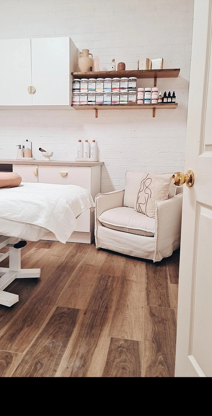 A treatment room with a made-up bed, an armchair and shelves of product
